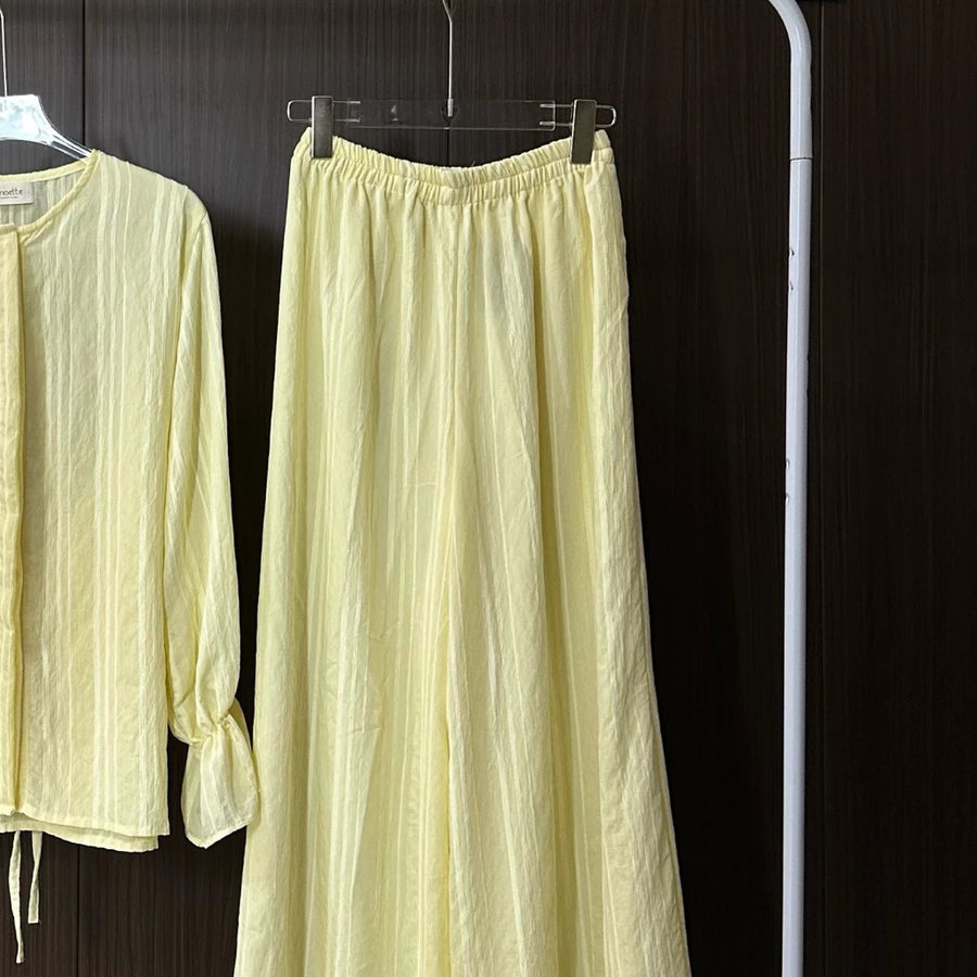 Light yellow long-sleeve top and wide-leg pants by Renaette hanging on a rack against a dark background.