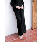 Person wearing a black pants by Renaette standing on a red-tiled floor against a white wall.