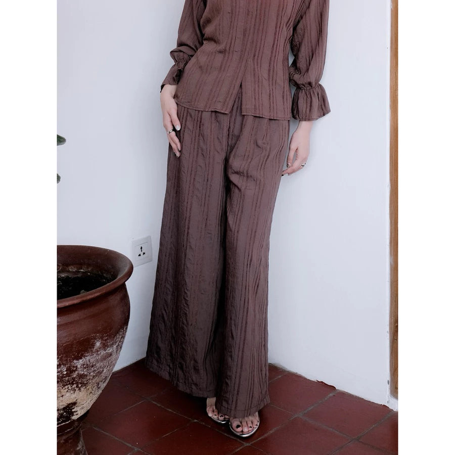 Person wearing a brown pants by Renaette standing against a white wall with a terracotta pot on the left.