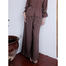 Person wearing a brown pants by Renaette standing against a white wall with a terracotta pot on the left.