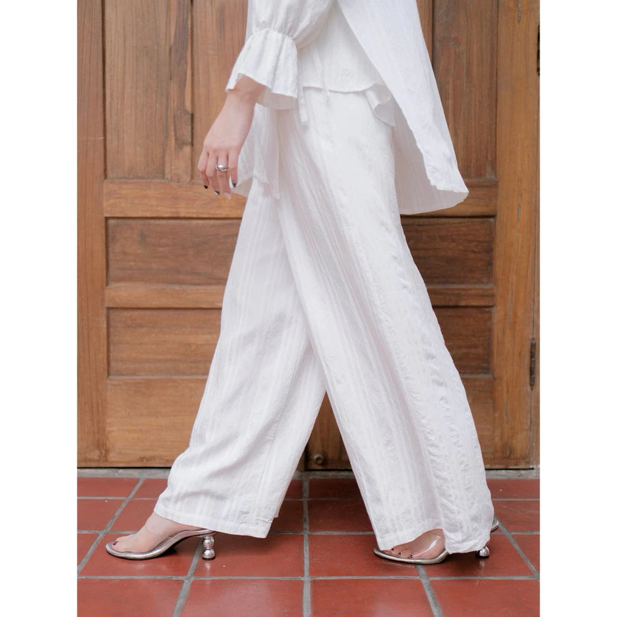 Person wearing a white wide-leg pants by Renaette in front of a wooden door.