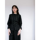 Woman wearing a black pleated blouse by Renaette against a white background