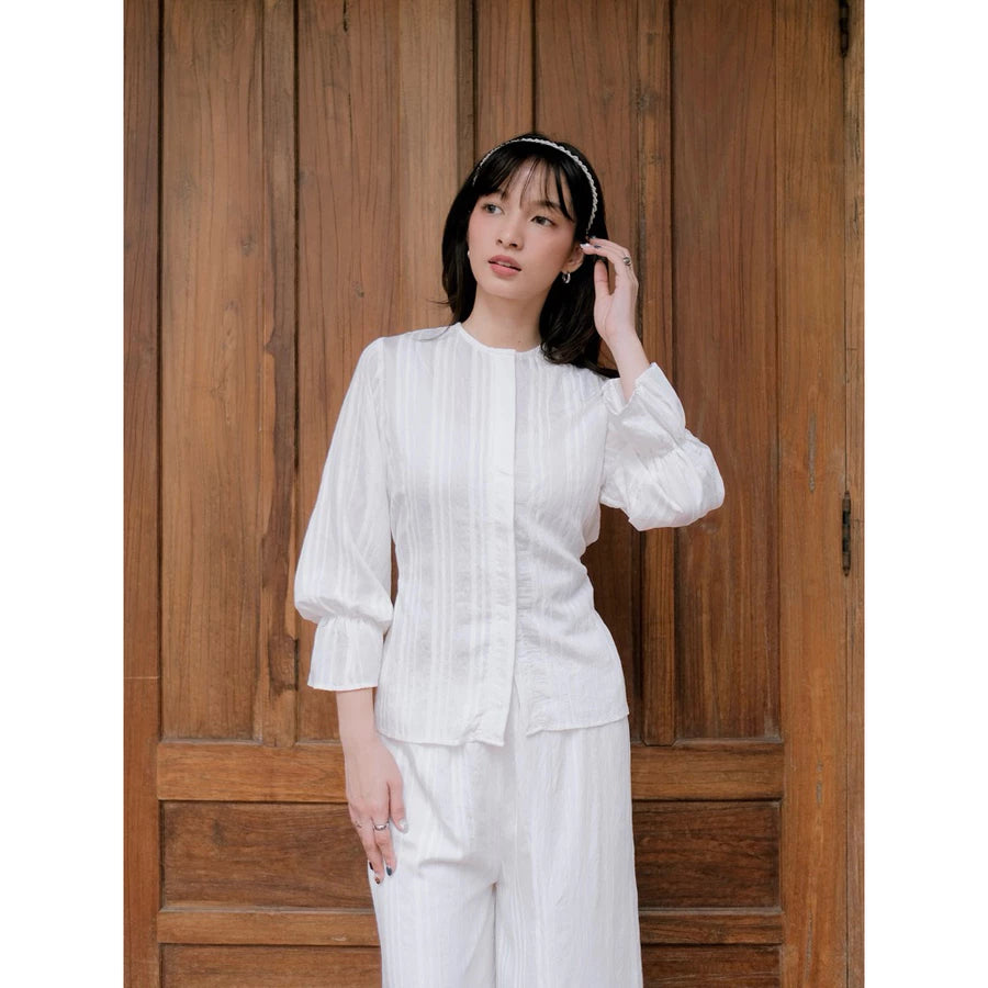 Woman in a white pleated blouse by Renaette standing in front of a wooden door