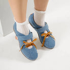 Blue flat shoes with strap and brown laces by Dianable worn with white socks on a light background