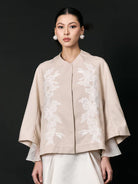 Woman wearing a beige embroidered jacket with white accents by Studio Tui on a black background