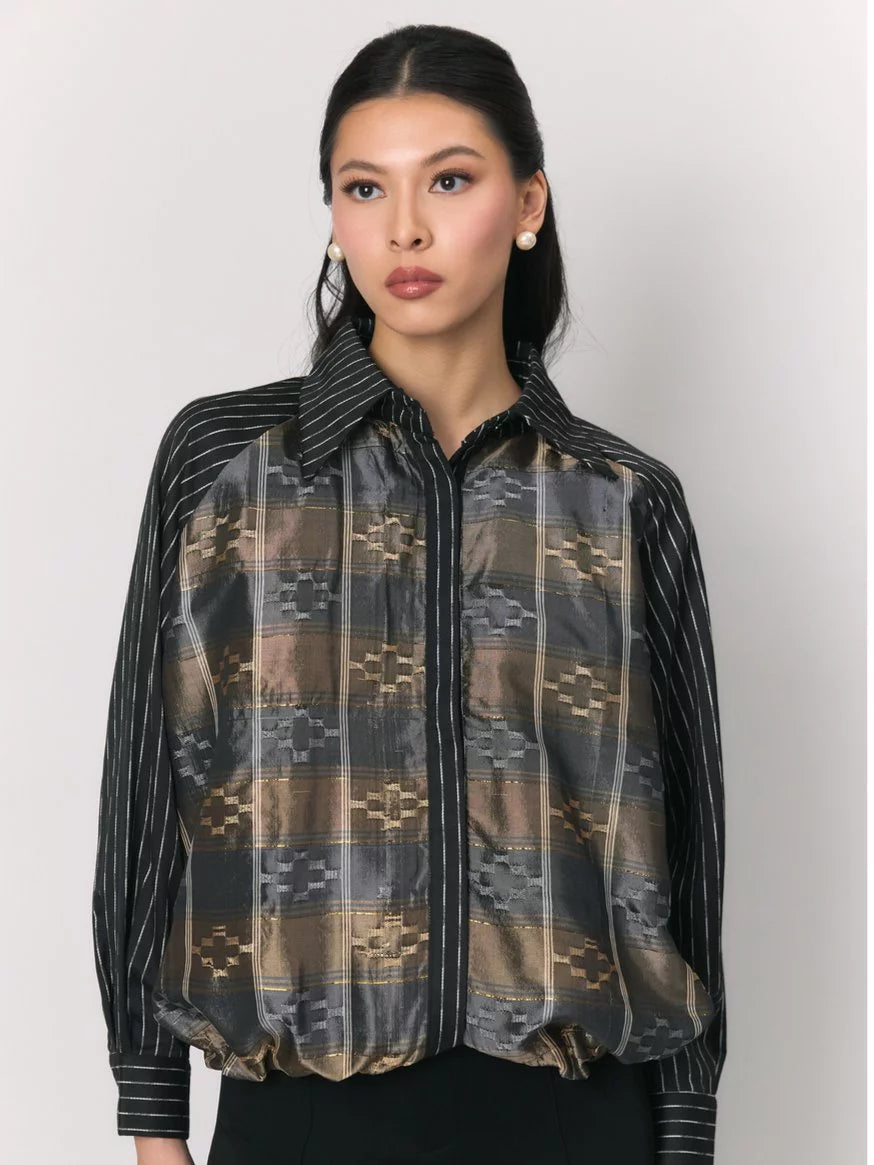 A woman modeling a sheer long-sleeve jacket by Studio Tui with a geometric plaid pattern in brown, beige, and gray, paired with black pinstriped sleeves and a black collar.