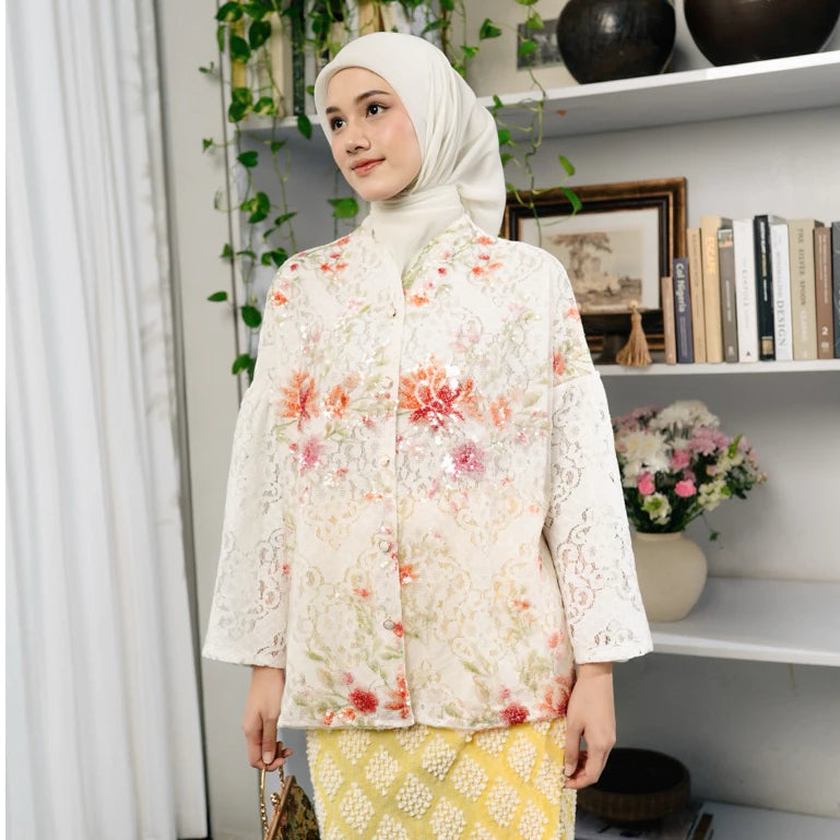 Woman wearing a white floral lace top by Haidee Orlin in a room with shelves and plants