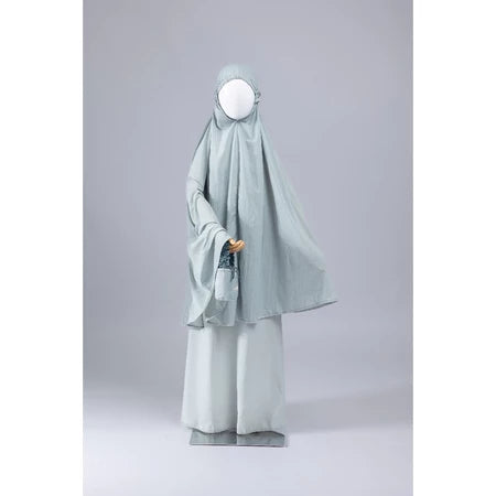 Mannequin wearing a light green mukena for kids from Muhajir Project on a gray background