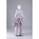 Mannequin wearing a light purple mukena for kids from Muhajir Project on a gray background
