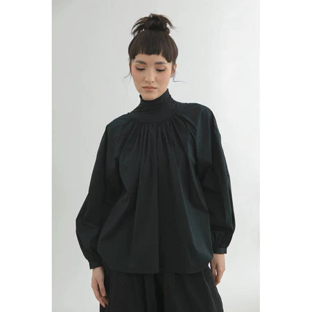 Person wearing a black blouse by Yestoday with a high collar against a white background
