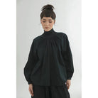 Person wearing a black blouse by Yestoday with a high collar against a white background