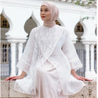 A woman wearing a white shirt with lace details by Casa Elana and a maxi skirt, standing in front of a building with arches.