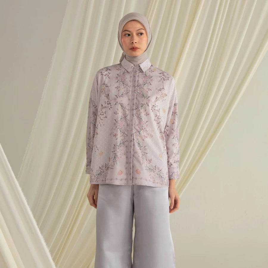 Person wearing a purple floral shirt by Hijabchic and light gray pants against a draped fabric background