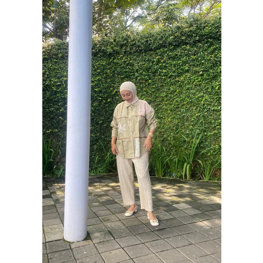 Woman wearing a striped shirt by Abame with olive-colored line accents, holding a coffee cup on a white background