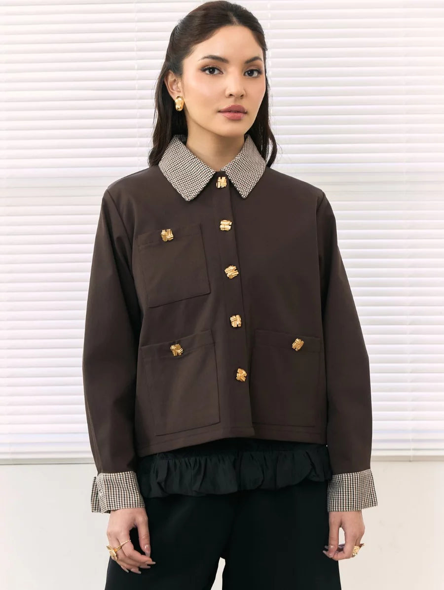 A woman models a dark brown cropped jacket by Studio Tui featuring a textured gray and white patterned collar and cuffs, adorned with gold-tone decorative buttons, set against a background of white window blinds.