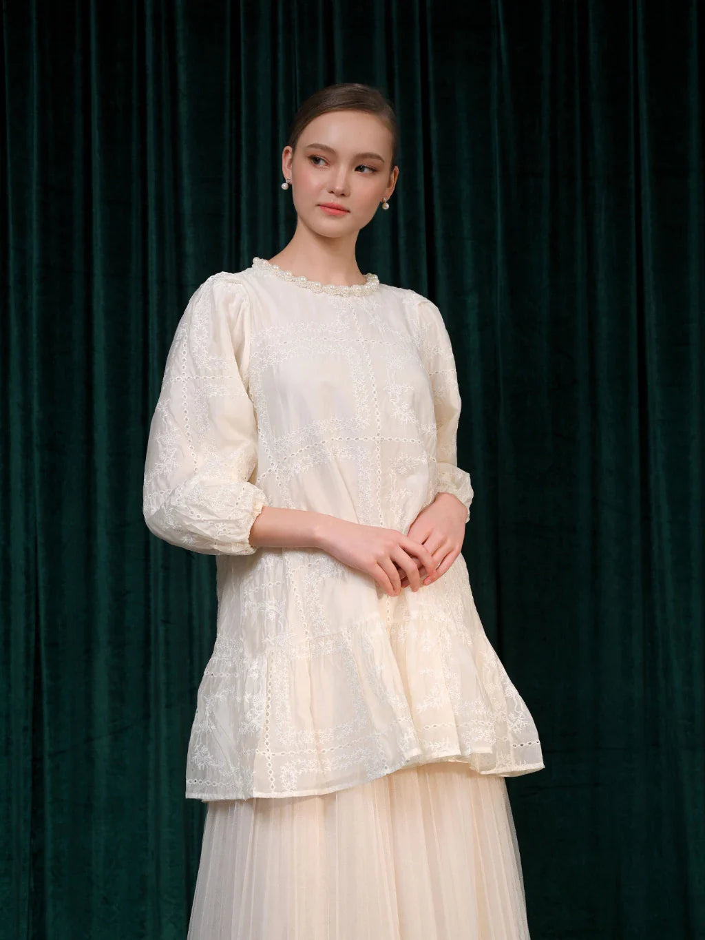 A woman wearing a beige tunic with long sleeves and a round neckline, paired with a pleated skirt.

Seorang wanita memakai tunik berwarna beige berlengan panjang dengan kerah bulat, dipadukan dengan rok pleated.