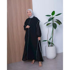 Woman in a black dress by Abame standing next to a plant indoors