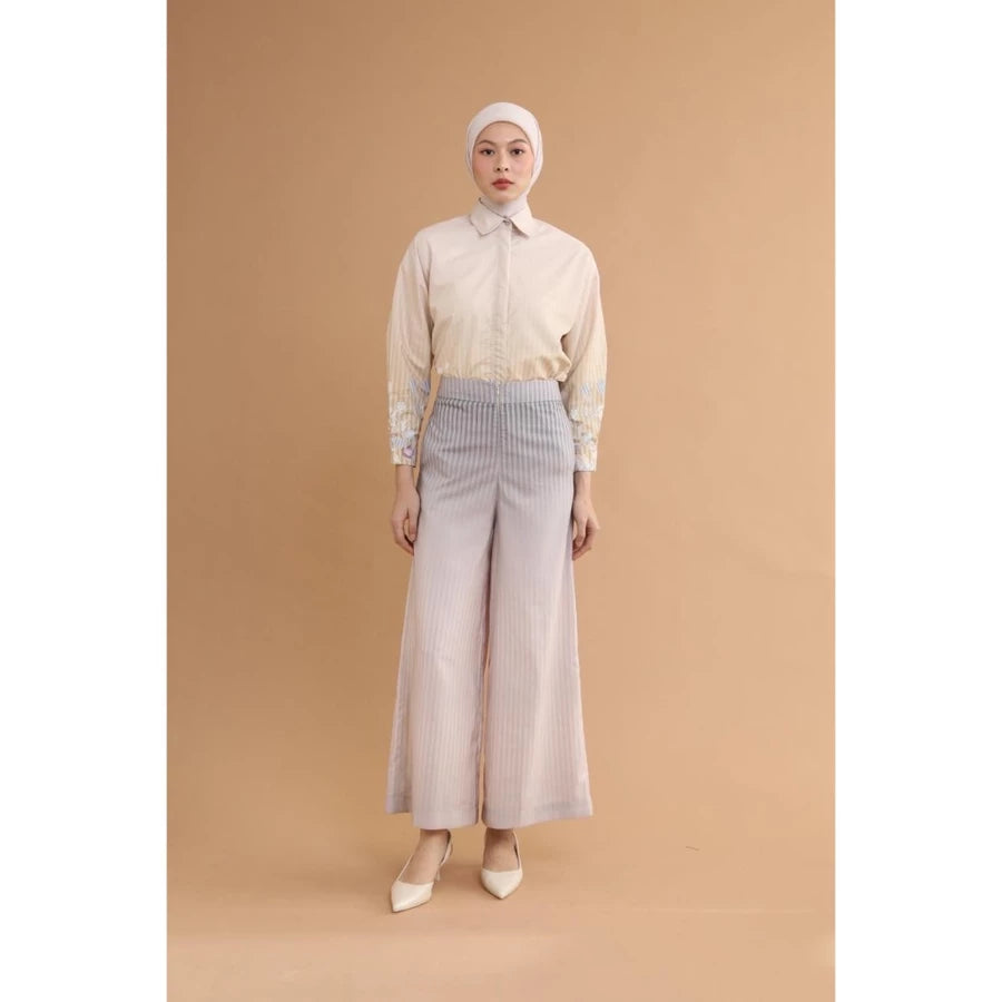 Woman wearing a cream blouse and violet wide-leg pants by Haidee Orlin against a brown background