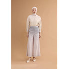 Woman wearing a cream blouse and violet wide-leg pants by Haidee Orlin against a brown background