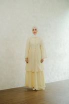 Woman wearing a light yellow tunic by Tufine and hijab against a white wall.

Seorang wanita yang mengenakan tunik berwarna kuning muda dari Tufine dan jilbab, berlatar belakang dinding putih.