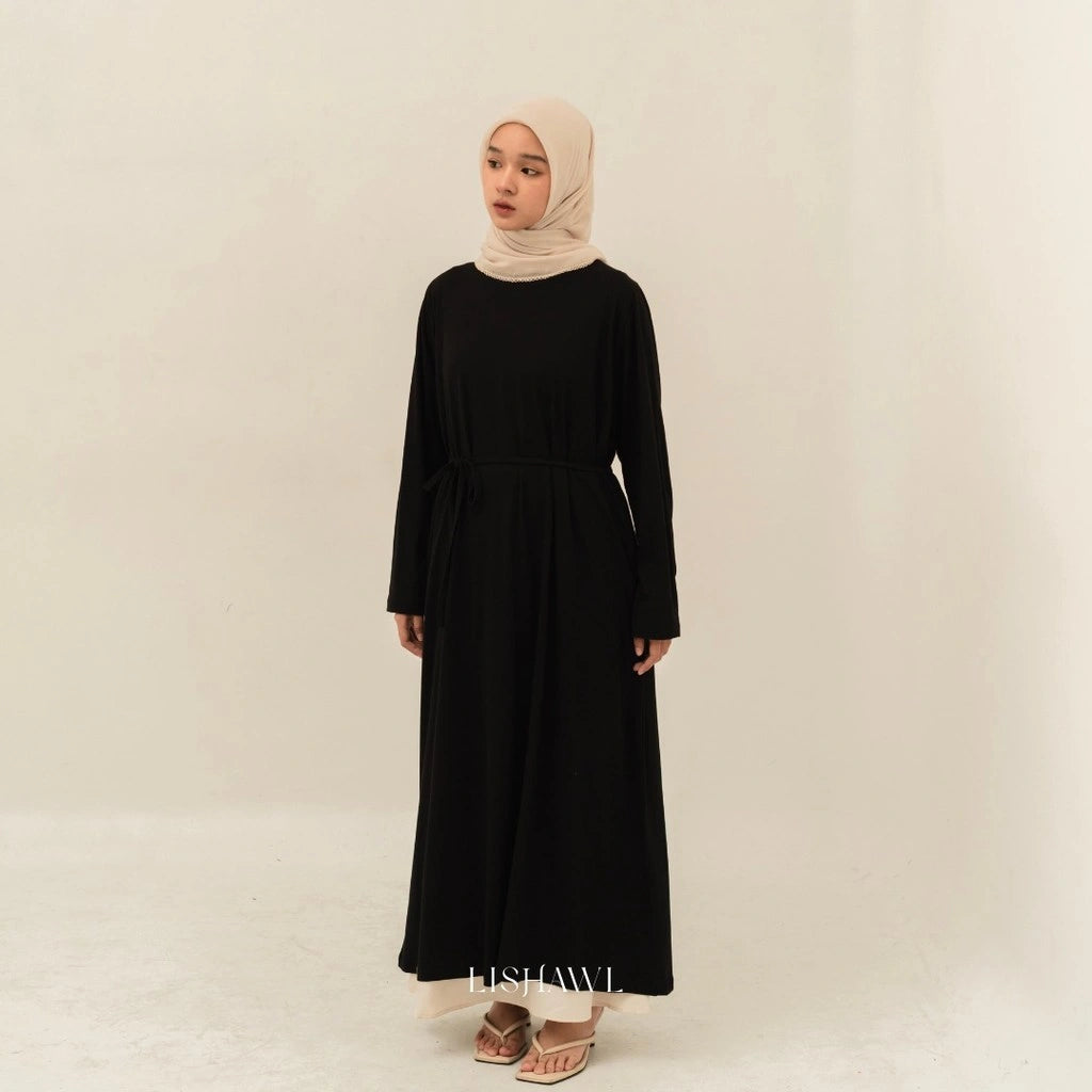 Woman wearing a black dress by BWBYAZ and beige hijab on a plain background