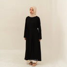 Woman wearing a black dress by BWBYAZ and beige hijab on a plain background