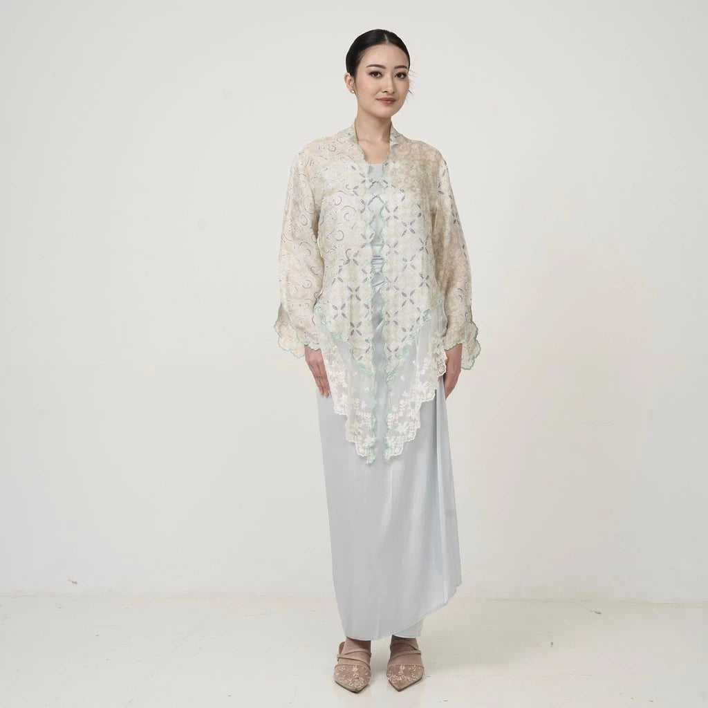 A woman wearing an ivory Kebaya by Kartinis Label with long bell sleeves and front button design, standing against a white background.