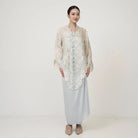 A woman wearing an ivory Kebaya by Kartinis Label with long bell sleeves and front button design, standing against a white background.