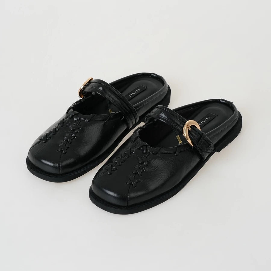 Pair of black mules sandals by Cekhas with gold buckles on a white background