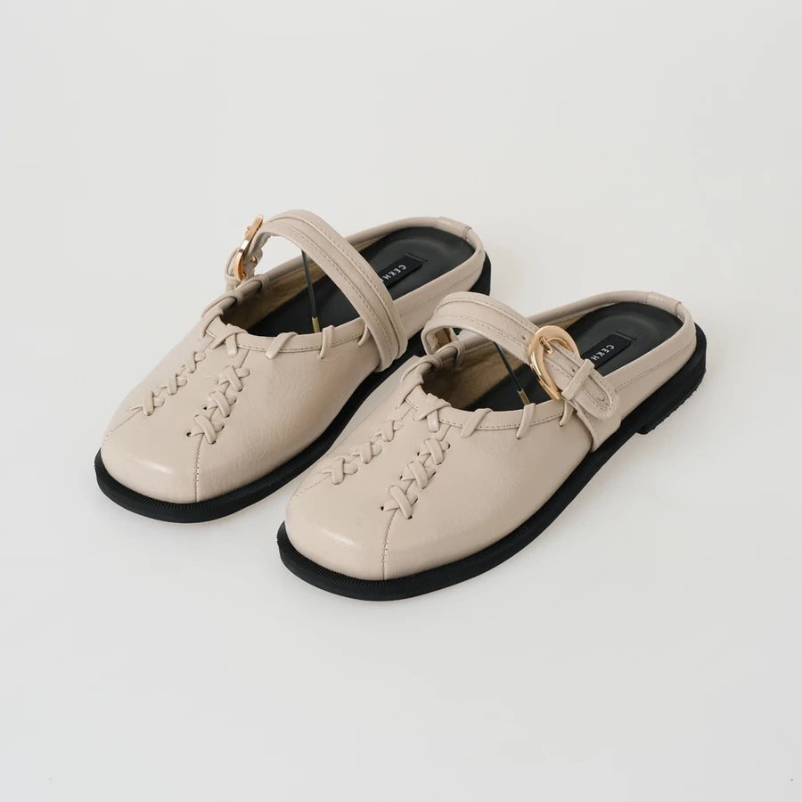 Pair of beige mules sandals by Cekhas with black soles on a light gray background