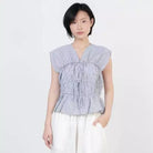 A model wearing a grey and white vertically striped peplum top by Kasyalia with ruffled details and white wide-leg pants, set against a plain light gray background.