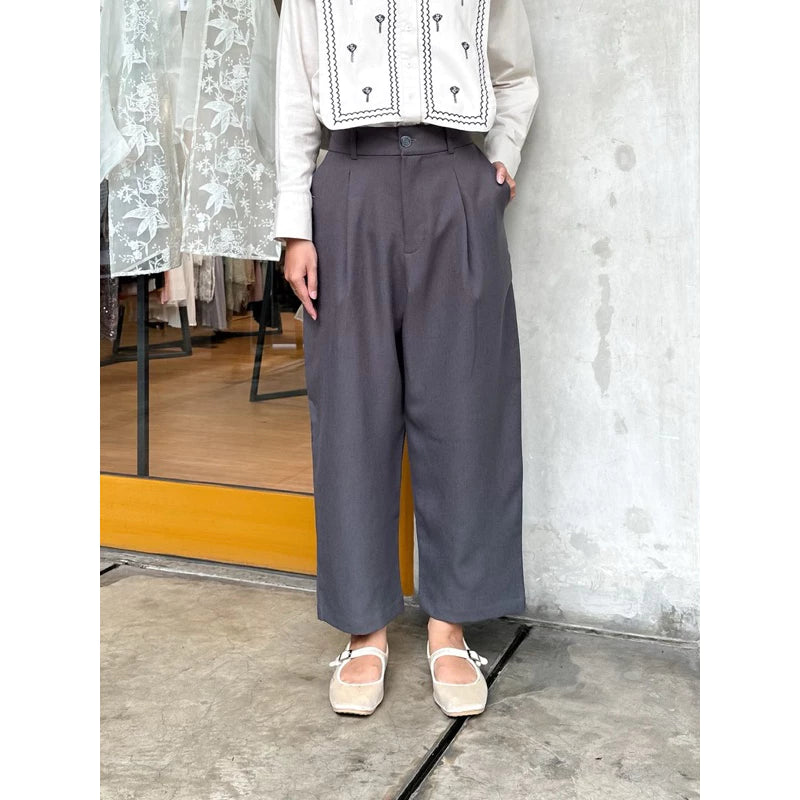 A person wearing dark grey pants by Maima and a patterned top, with their feet visible in flat shoes.