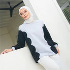 Woman wearing a white and black patterned sweater by Casa Elana with a hijab, sitting on a white surface.