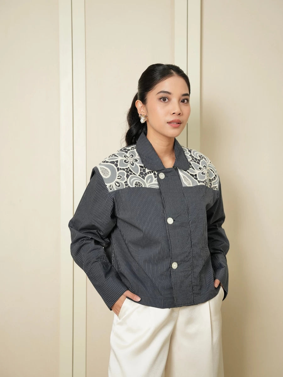 Woman wearing a gray women’s jacket by Studio Tui featuring contrasting floral panel details on the shoulders, paired with wide-leg white trousers for an elegant semi-formal look.