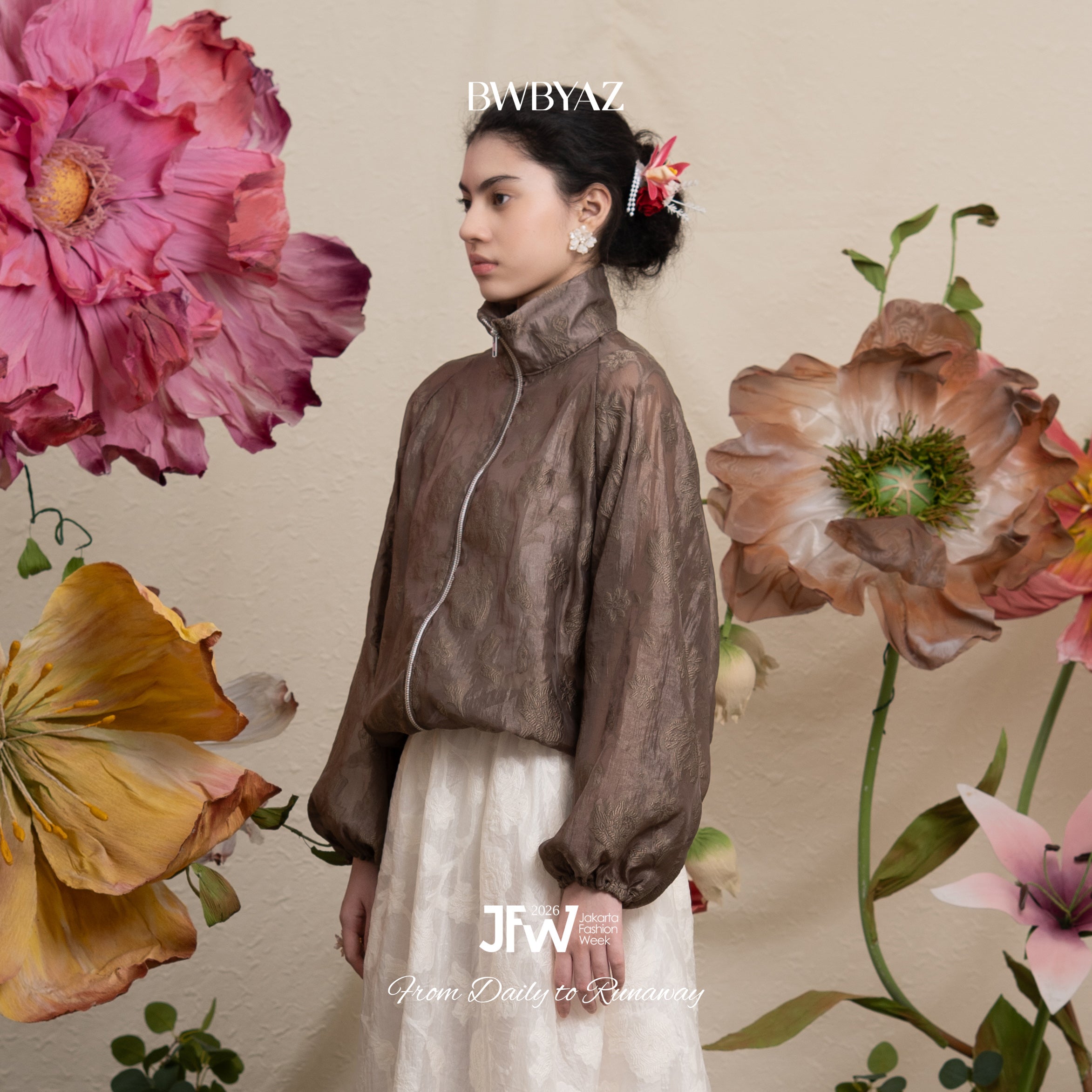 Woman in a dark brown floral-patterned lace jacket and white pants standing among large flowers with 'BWBYAZ' branding.