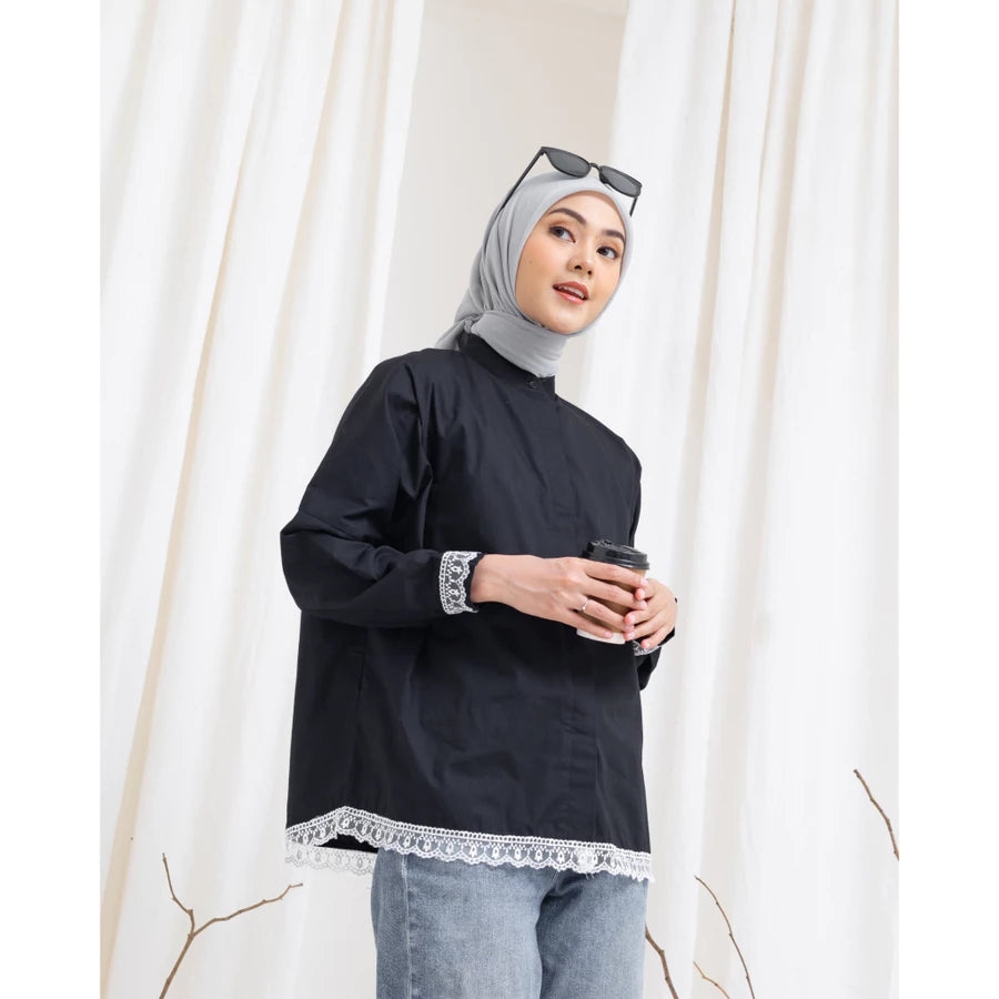 Woman wearing a black shirt by Abame with lace trim and gray hijab, holding a coffee cup against a white curtain background.