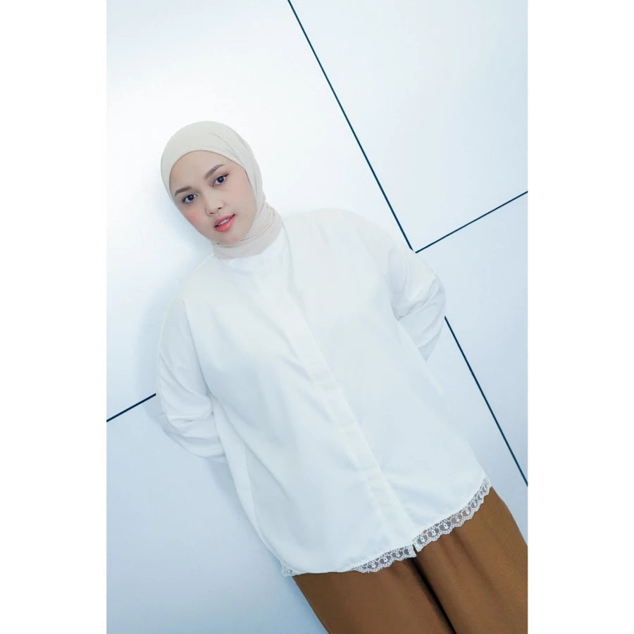 Woman wearing a white hijab and white shirt by Abame with brown pants on a light blue background