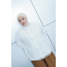 Person wearing a white long-sleeve shirt by Abame with lace trim on a light blue background