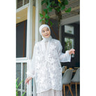 Woman wearing a white lace outer by Casa Elana standing in front of a building entrance.