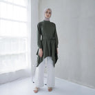 A woman wearing a green tunic with a semi turtleneck, sleeve pleats, and an detachable belt, paired with white pants.