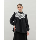 Woman wearing a black blouse by Kasa Heritage with lace detailing on a light gray background