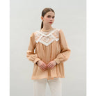 Woman wearing a beige blouse by Kasa Heritage with lace details on a plain background