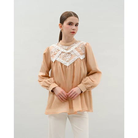 Woman wearing a beige blouse by Kasa Heritage with lace details on a plain background