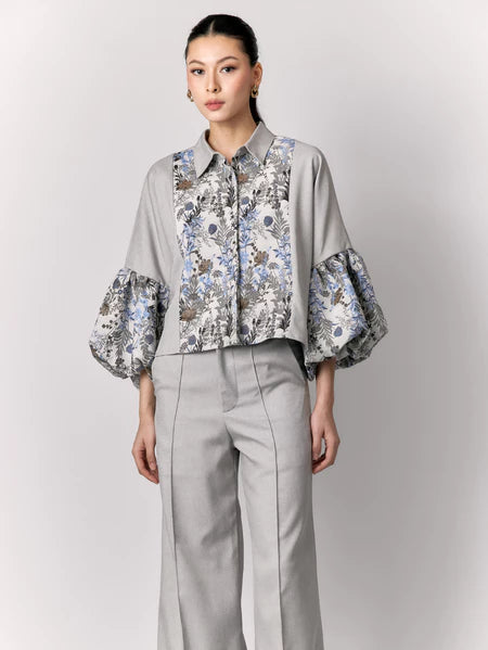 Woman wearing a gray outer by Studio Tui with floral cuffs and a matching skirt on a light gray background