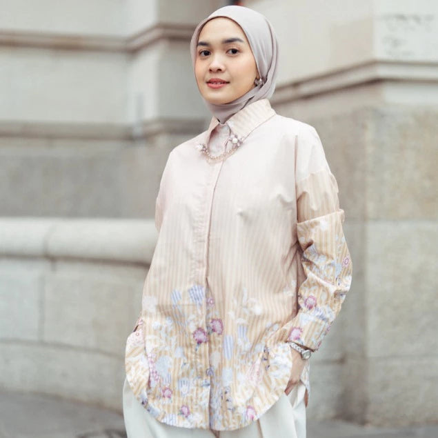 Woman wearing a light-colored floral blouse by Haidee Orlin against a neutral background