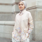 Woman wearing a light-colored floral blouse by Haidee Orlin against a neutral background