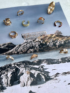 Gold rings by Darje displayed on a piece of paper with a scenic background