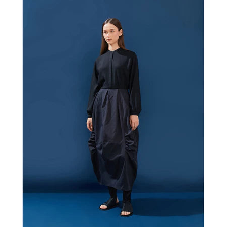 Woman wearing a black top and black pleated skirt by Yestoday against a blue background