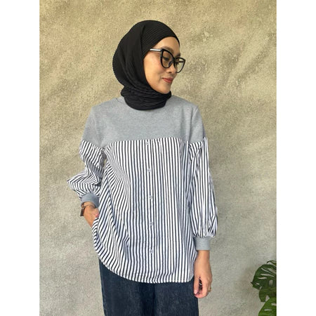 Woman wearing a gray and black striped shirt by Casa Elana with a hijab against a textured wall.