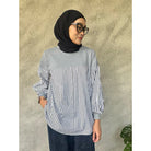 Woman wearing a gray and black striped shirt by Casa Elana with a hijab against a textured wall.